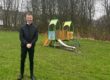 Mayor-Cllr-Curtis-Bihari in a black jacket stands on grass in front of a small, colourful playground structure.
