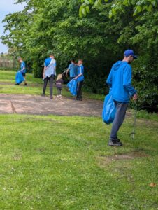Five people in blue pick up litter in a park, carrying large blue bags and litter pickers.