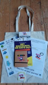 Canvas tote with quiz sheets, booklet, crayons, badge, and keyring on a wooden surface.