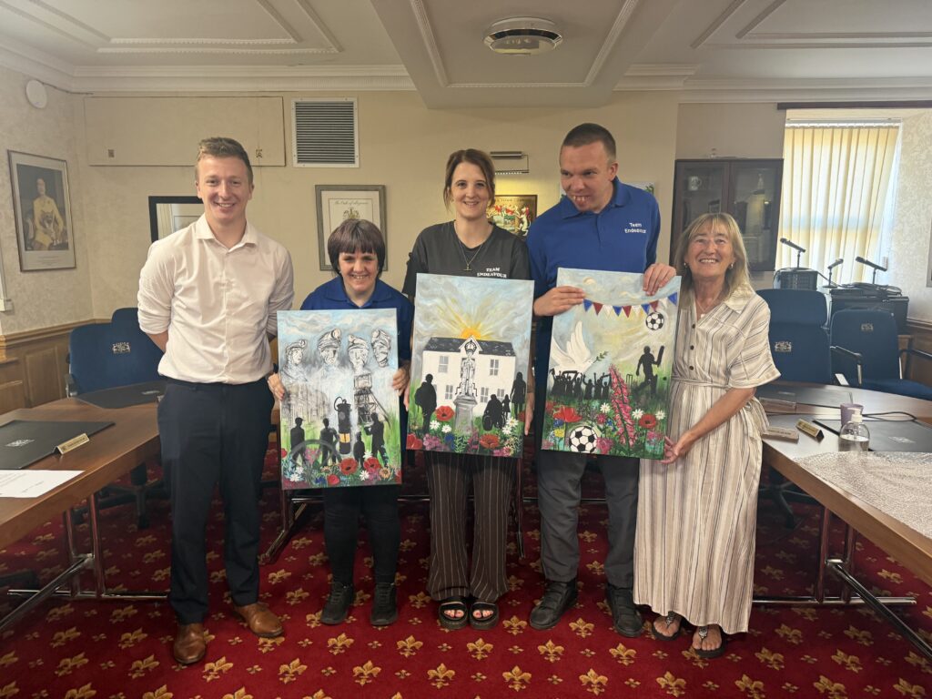 Five people indoors smiling and holding up colourful paintings in a formal meeting room.