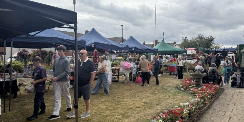 Stalls at Summer Gala 2026 People browsing stalls at an outdoor market, with flowers and marquees under a cloudy sky.