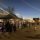 People gather at outdoor market stalls at dusk, with lights and traders under marquees.